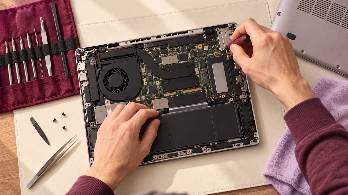 Hands inspect an open laptop with a set of precision tools.